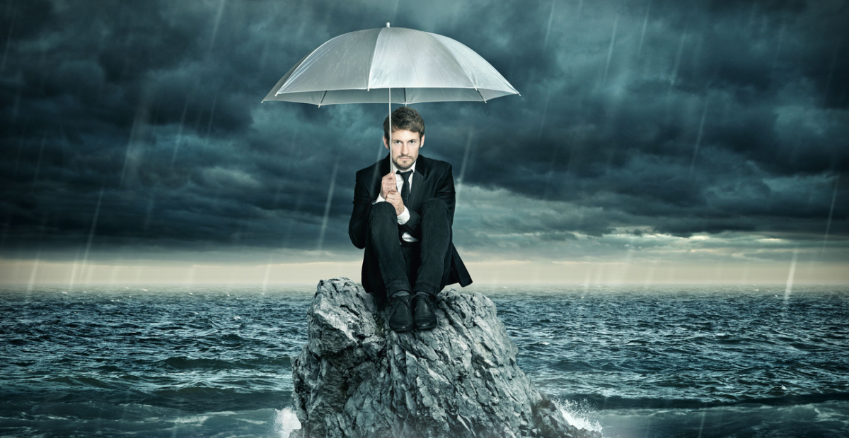 Man on rock huddled under umbrella