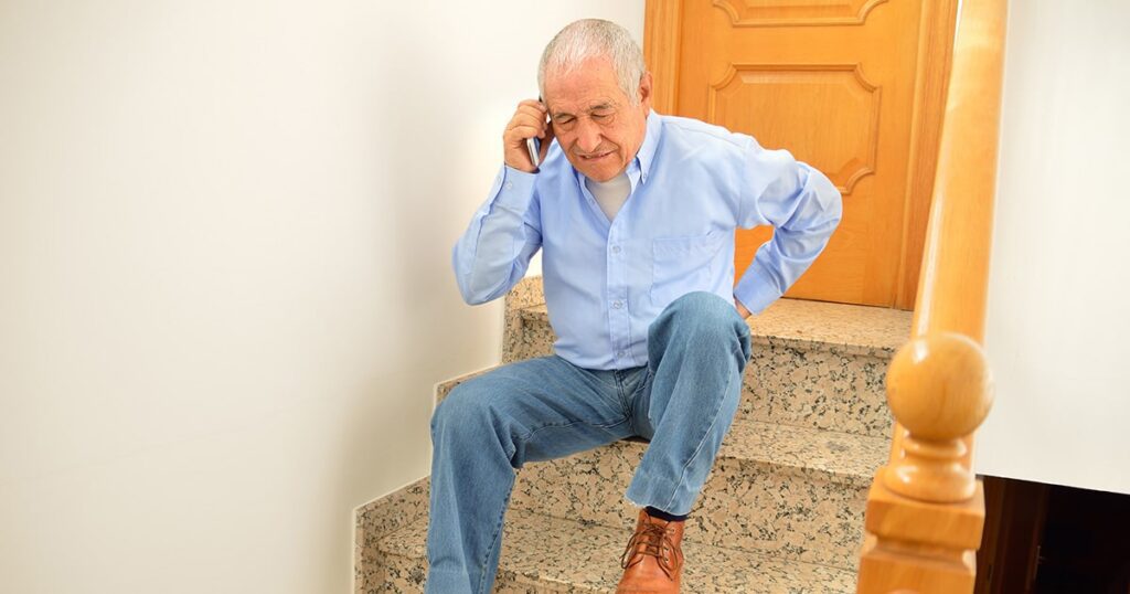 Man sitting on stairs holding back in pain on the phone