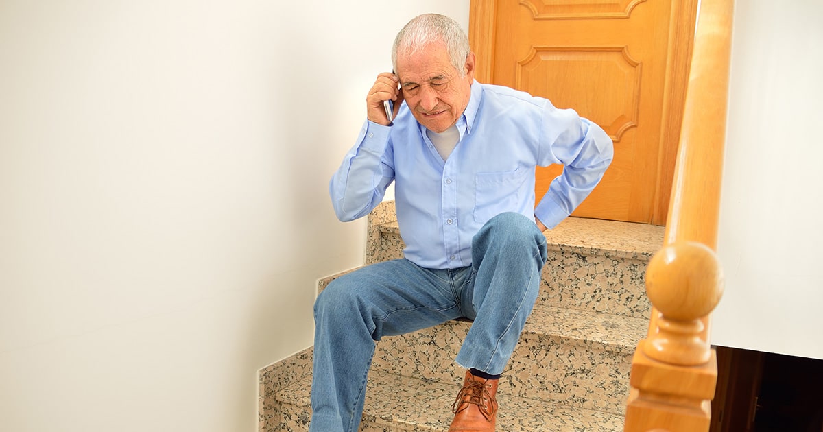 Man sitting on stairs holding back in pain on the phone