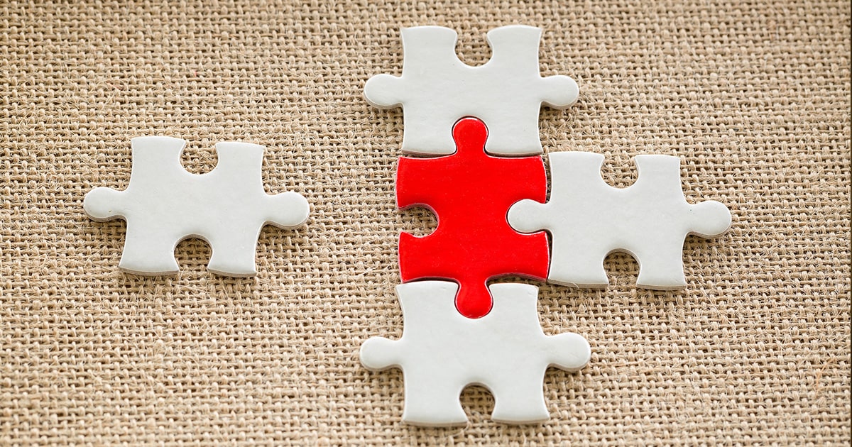 Red jigsaw piece in the middle of 4 other white jigsaw pieces with one broken off