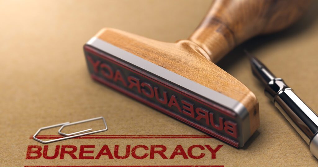 Stamp with Bureaucracy written on it next to a pen