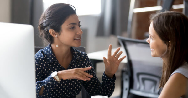 Two women discussing work at a computer desk