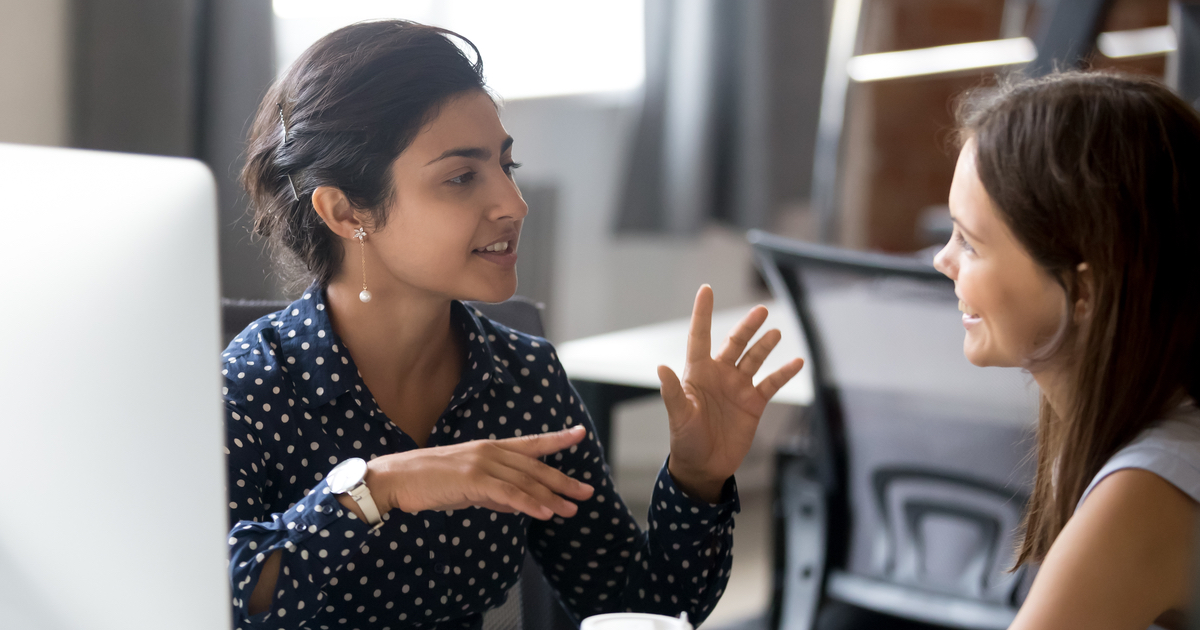 Two women discussing work at a computer desk