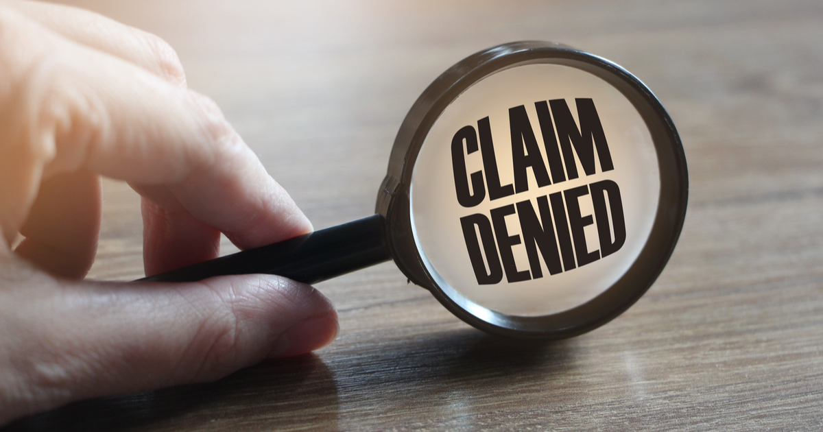 Hand holding magnifying glass with Claim Denied written
