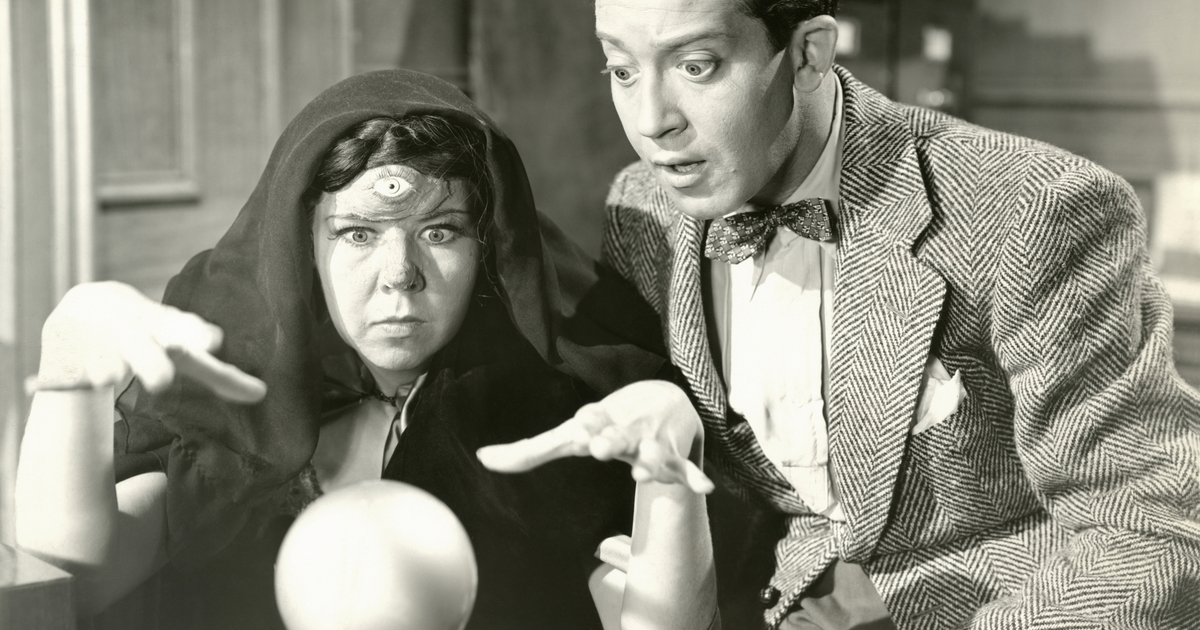 A fortune teller gesturing toward a crystal ball with a man standing behind her