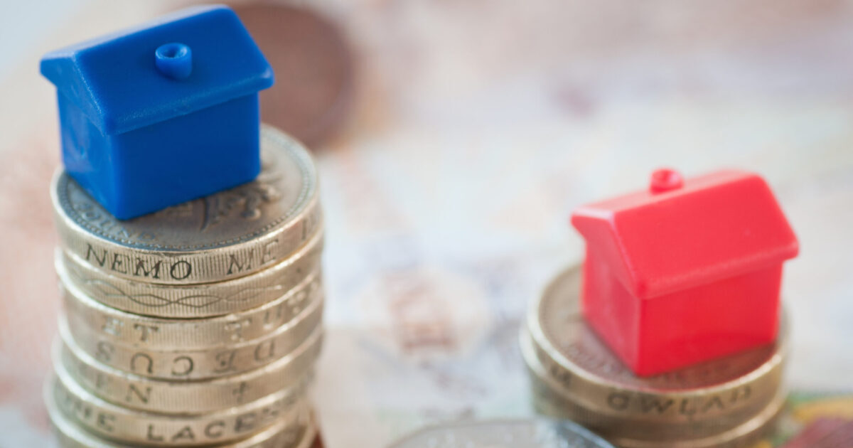 Blue and red house figures sitting on stacks of coins