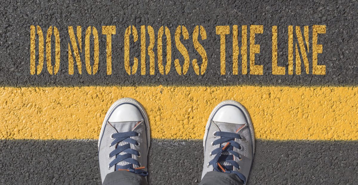 Sneakers standing before a yellow line with writing 'Don't Cross the Line'
