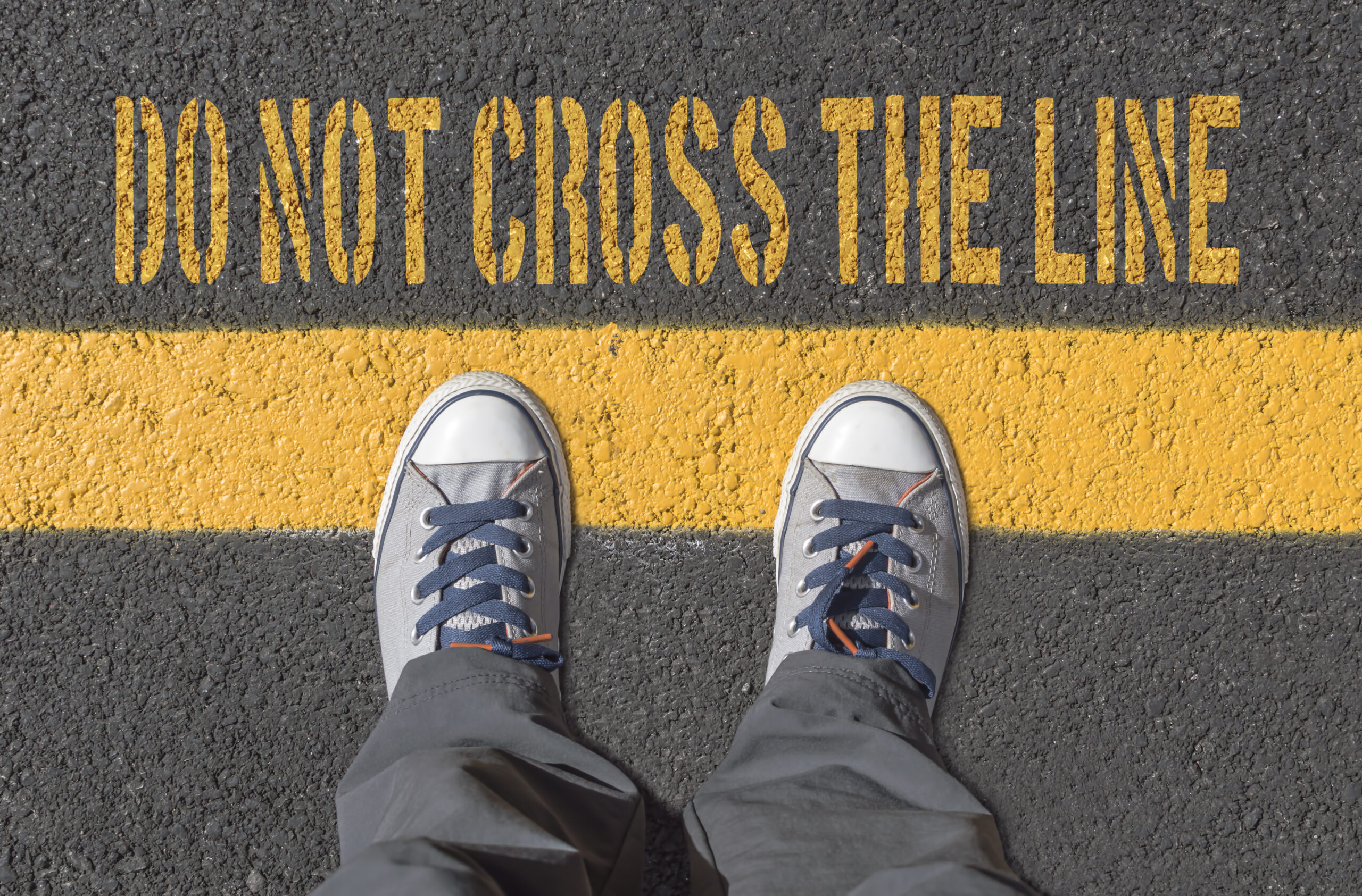 Sneakers standing before a yellow line with writing 'Don't Cross the Line'