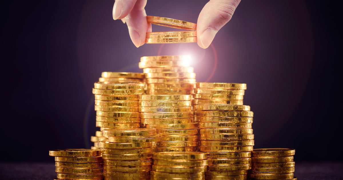 Gold coins being stacked with a hand taking some away