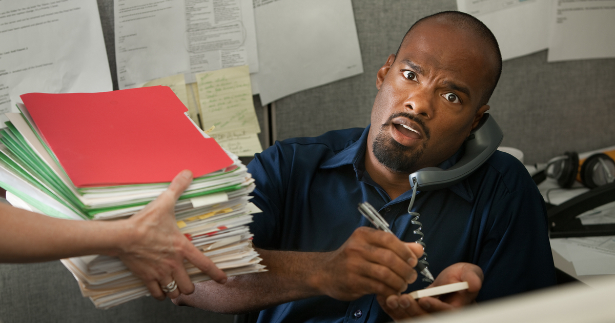 Man on the phone writing a note with more papers being handed to him