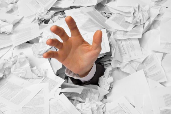 Hand reaching out from under a mountain of papers