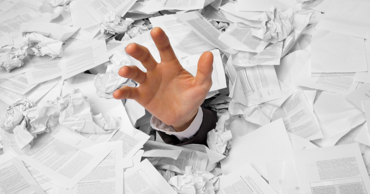 Hand reaching out from under a mountain of papers